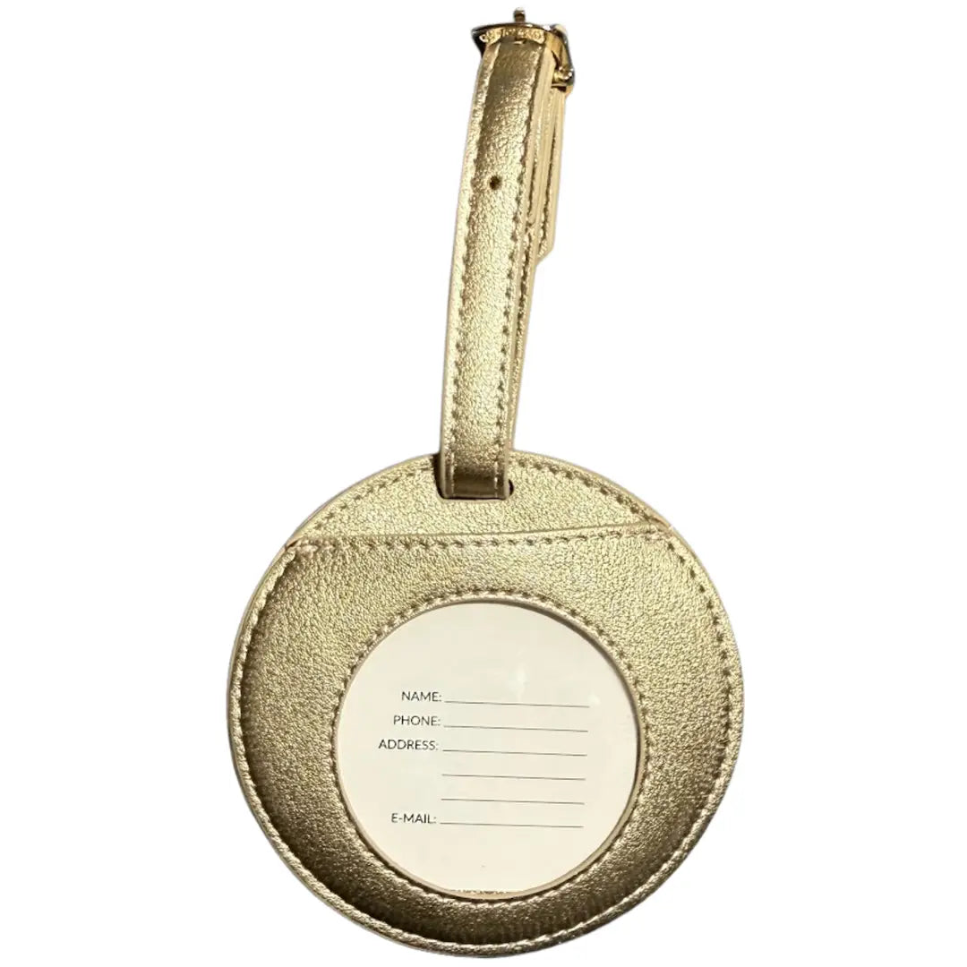 A round metallic gold luggage tag with a textured finish, featuring a central white circle with lines for writing personal details, and a matching gold strap at the top.