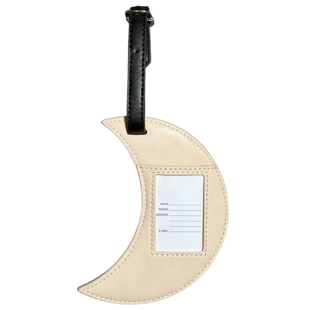 A crescent moon-shaped beige faux leather luggage tag with a black strap and a white name label on a plain white background.