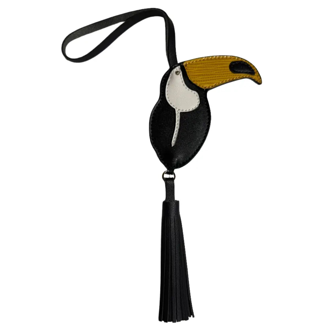 A black leather toucan-shaped luggage tag with a black strap, featuring a yellow and white beak and a long black tassel, shown on a plain white background.