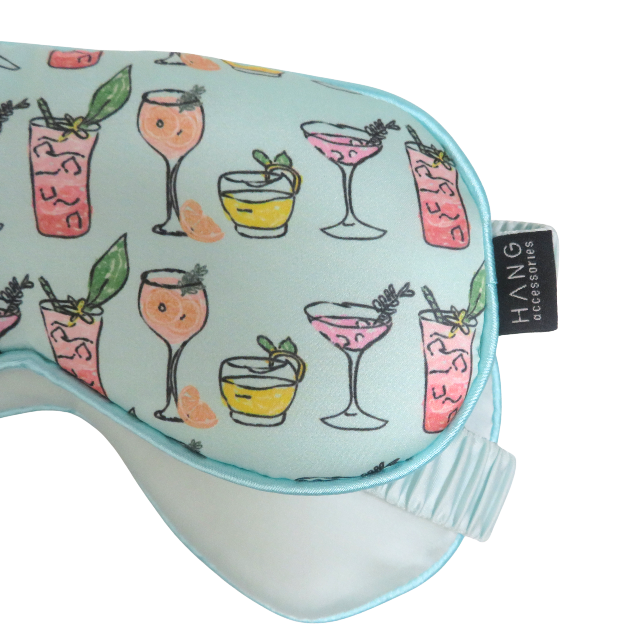 A close-up of a sleep mask with a light blue background and a pattern of colorful cocktail illustrations.