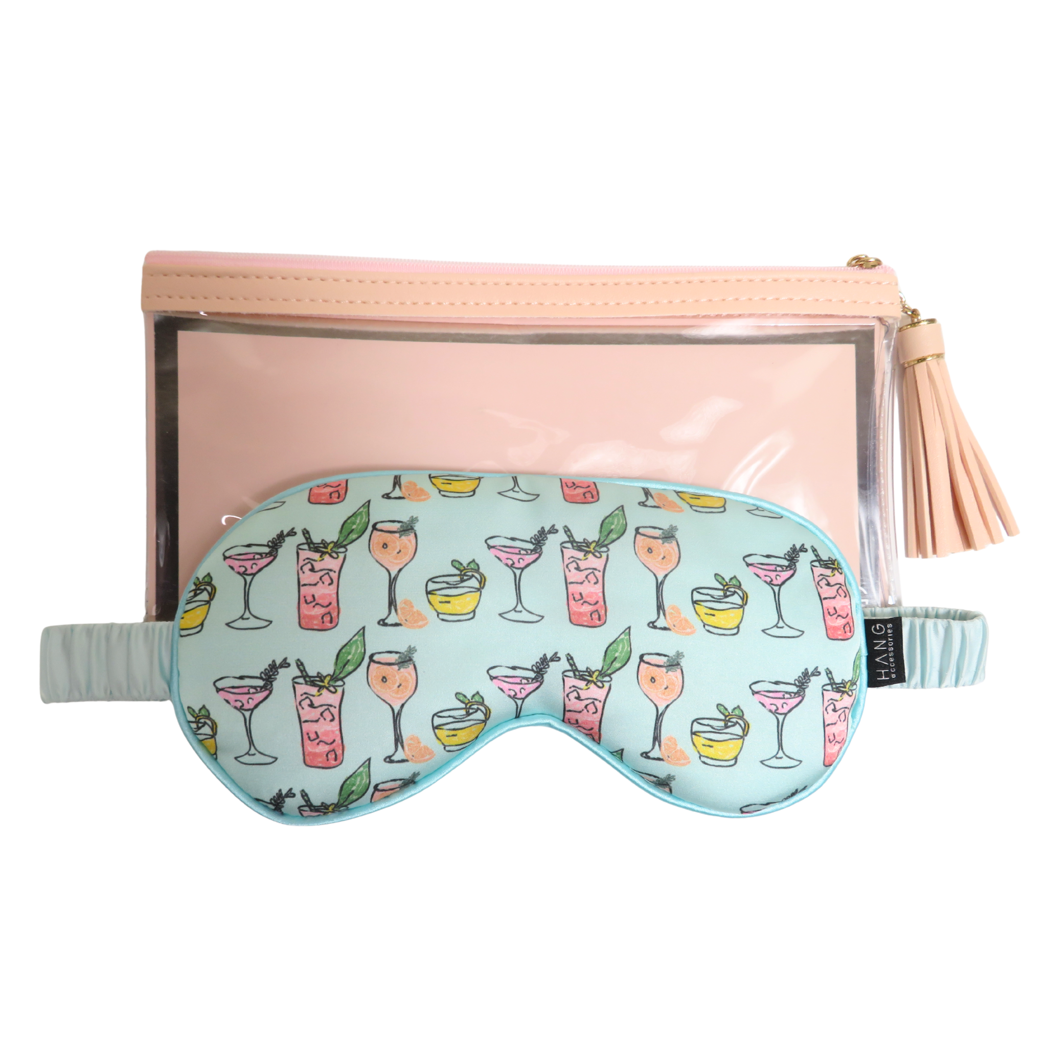 A light blue sleep mask with a colorful cocktail pattern, displayed in front of a peach zippered pouch with a clear window and tassel.