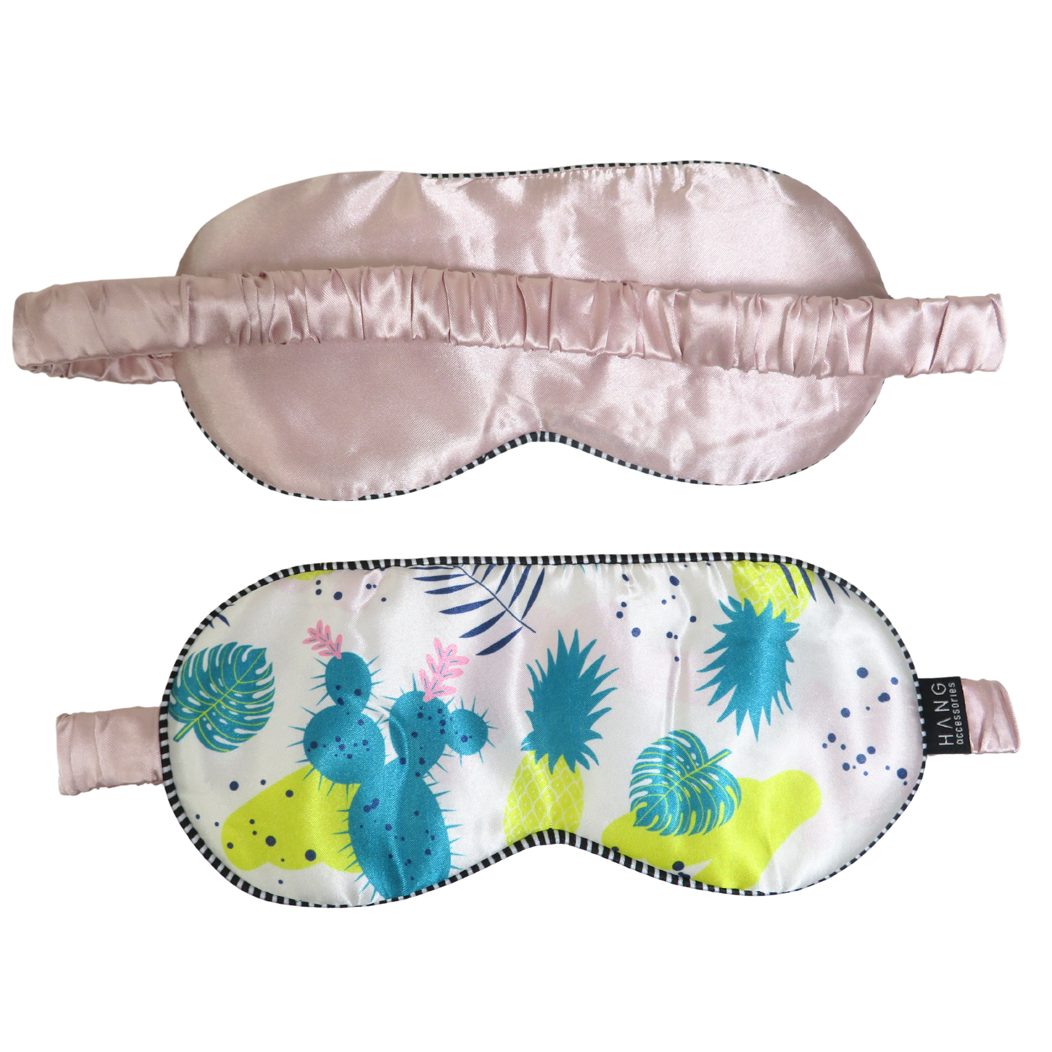 Two sleep masks shown on a plain white background: one in pale blush pink satin and one with a white base printed with turquoise, blue, yellow, and pink tropical/cactus motifs, both with elastic straps and black piped edges.