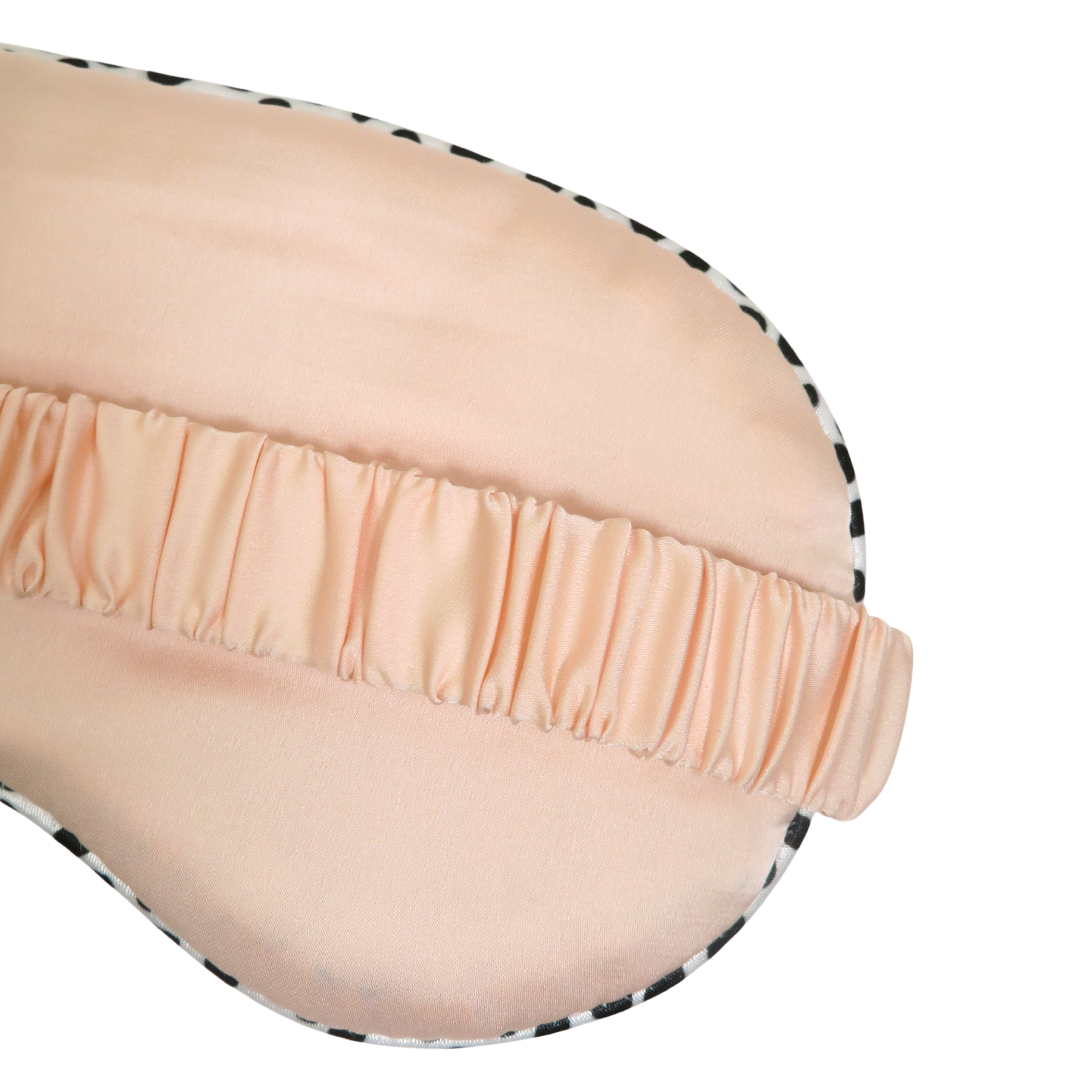 Close-up of a peach-colored satin sleep mask with a black and white patterned edge and an elasticized eye strap, shown on a white background.