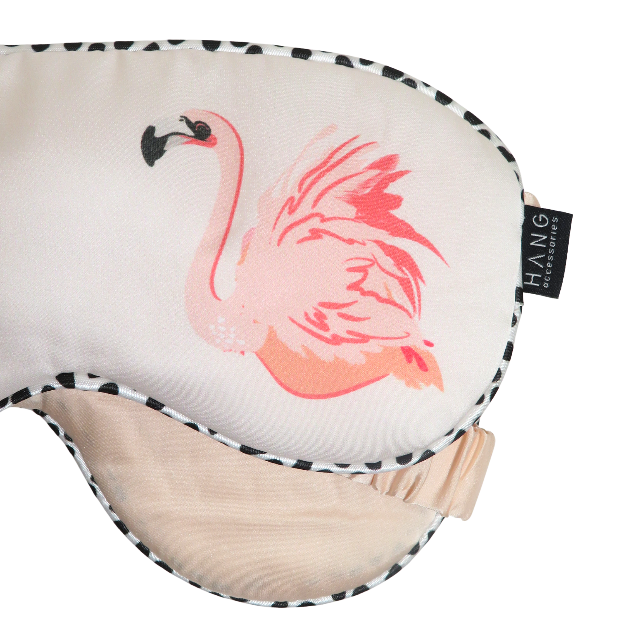 A close-up of a sleep mask with a pink flamingo illustration on a cream background, featuring a black and white spotted trim.