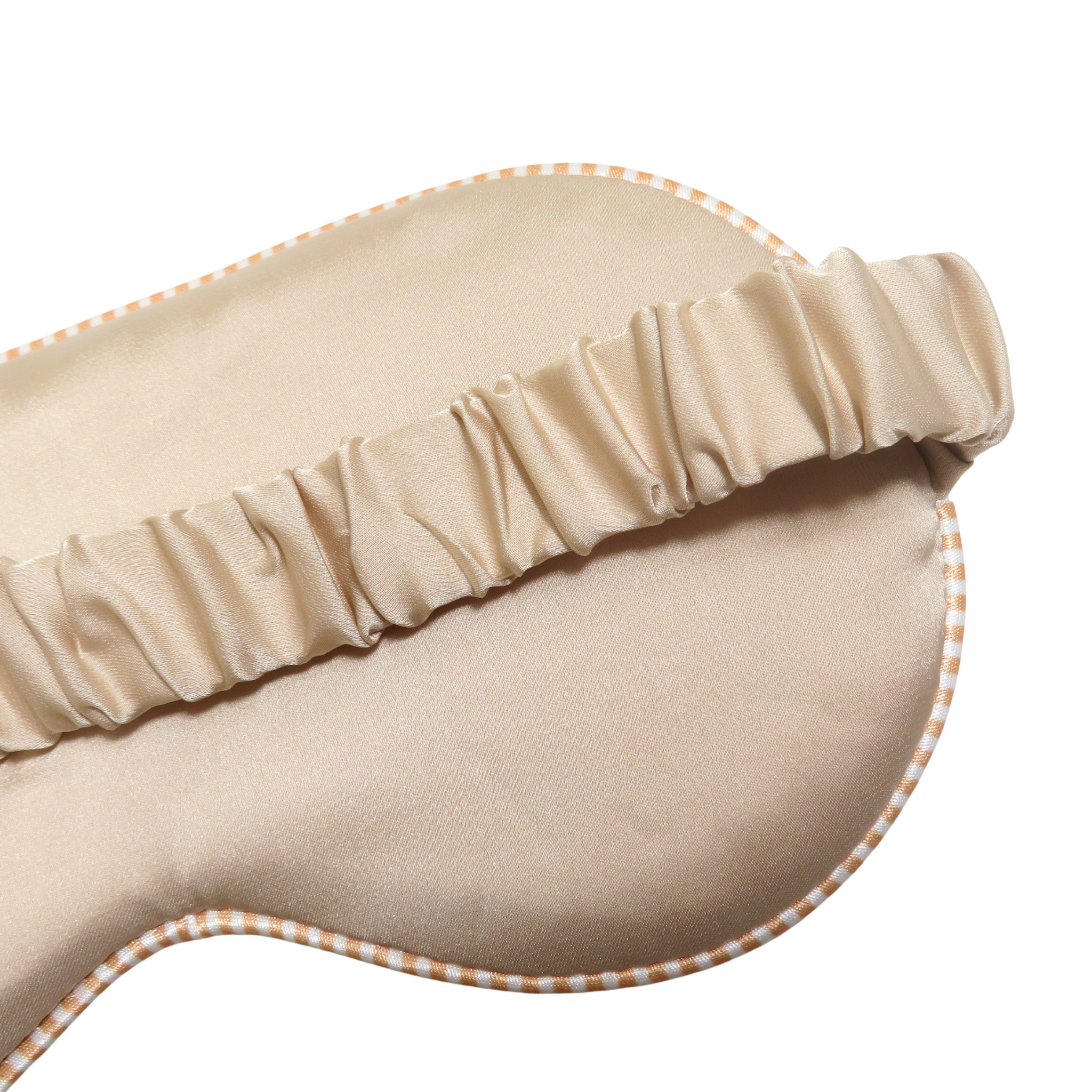 Close-up of a beige satin sleep mask with a gathered elastic strap and a subtle orange-and-white checkered edge, shown on a white background.