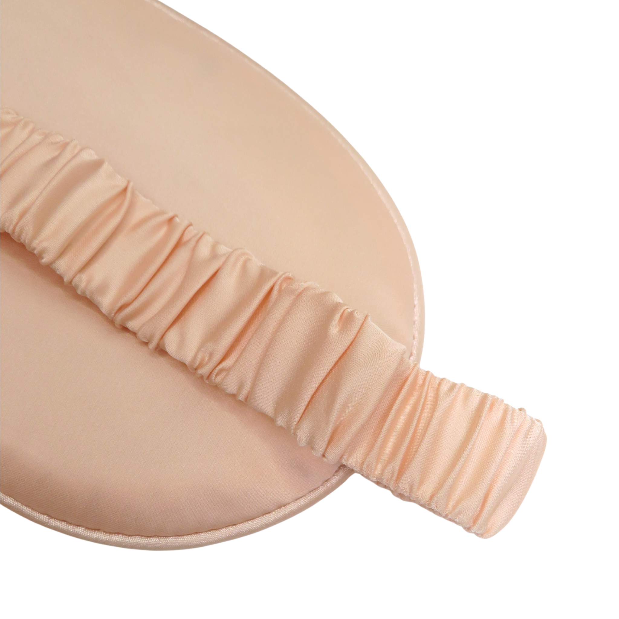 Close-up of a peach-colored sleep mask with a ruched elastic strap on a plain white background.