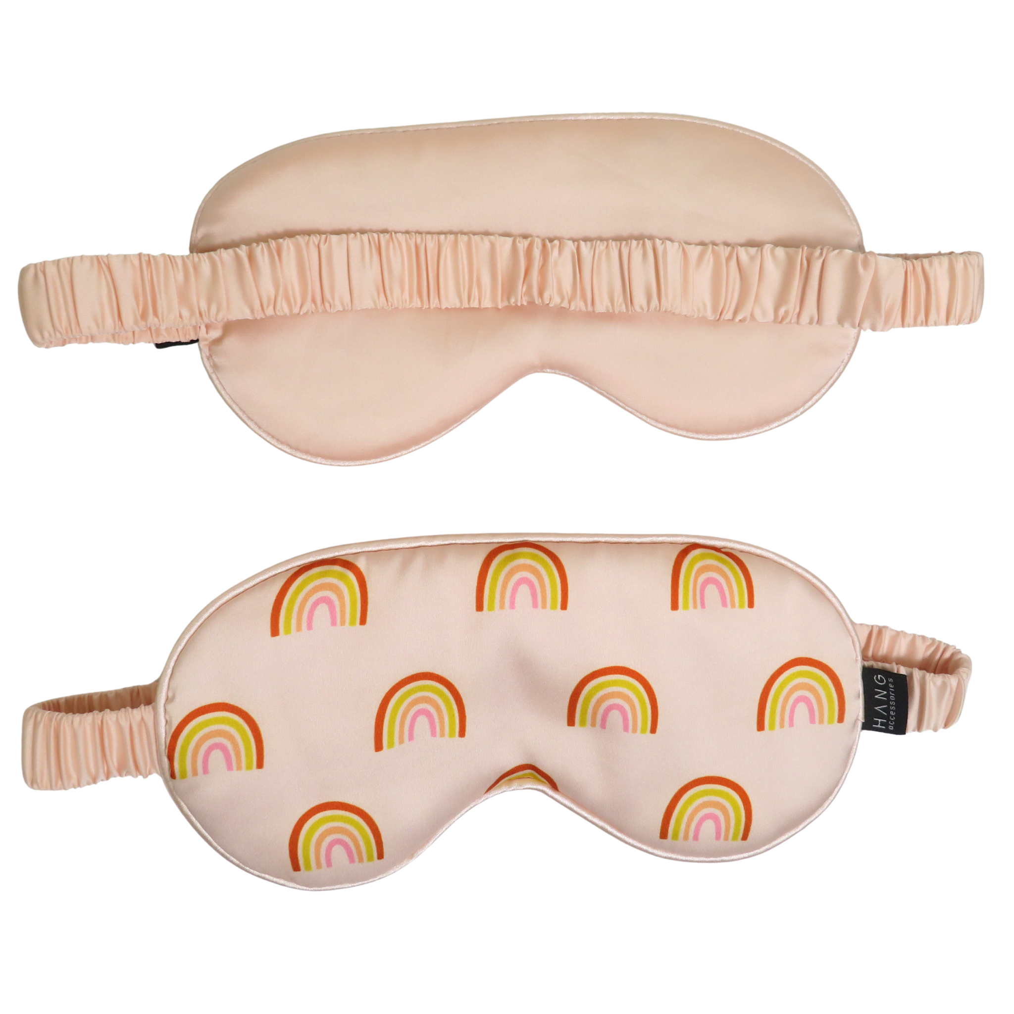 Two satin sleep masks on a white background, one solid pale blush pink and the other with a repeating rainbow pattern in pink, orange, yellow, and green on a pale pink base.