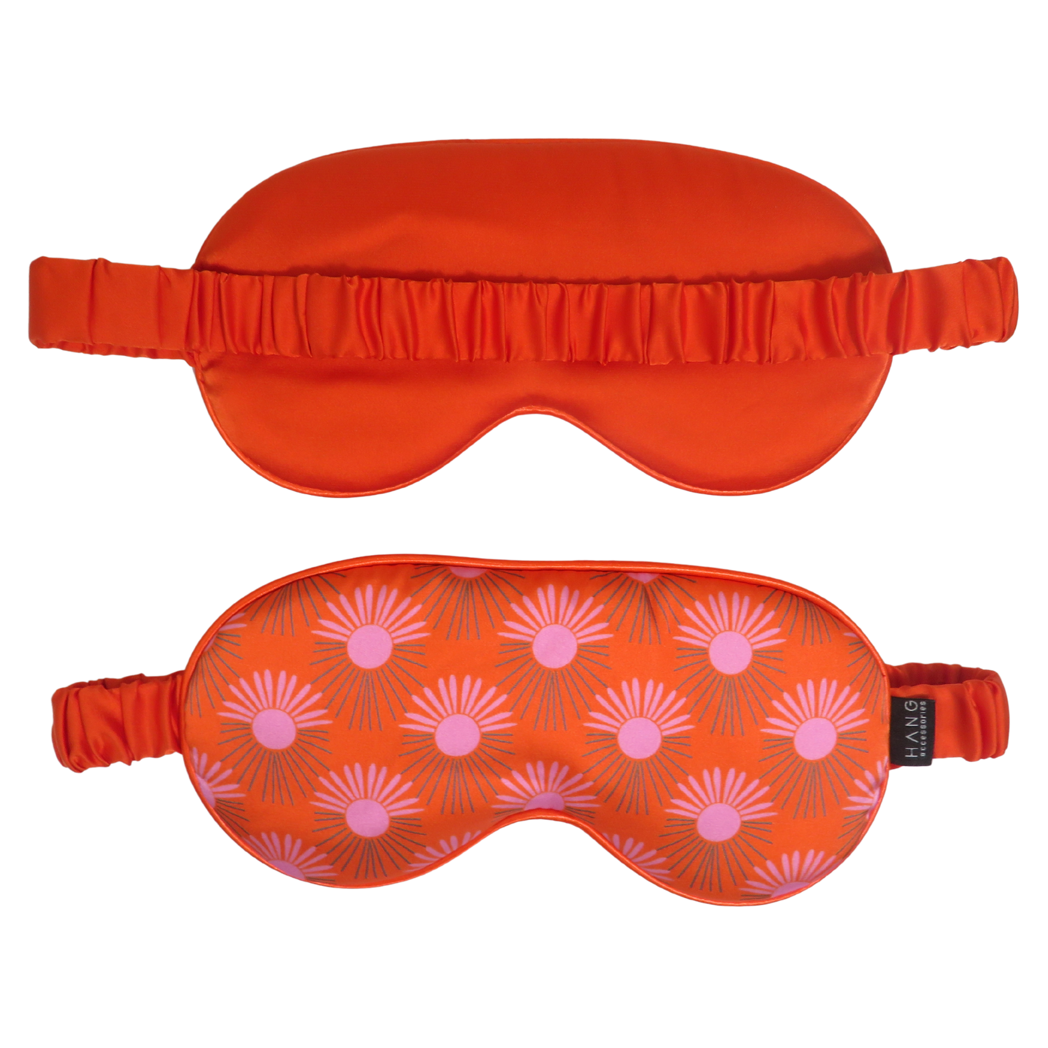 Two sleep masks on a plain white background: an orange satin mask with a ruffled edge at the top and an orange fabric mask with a pink and gray sunburst pattern below it.