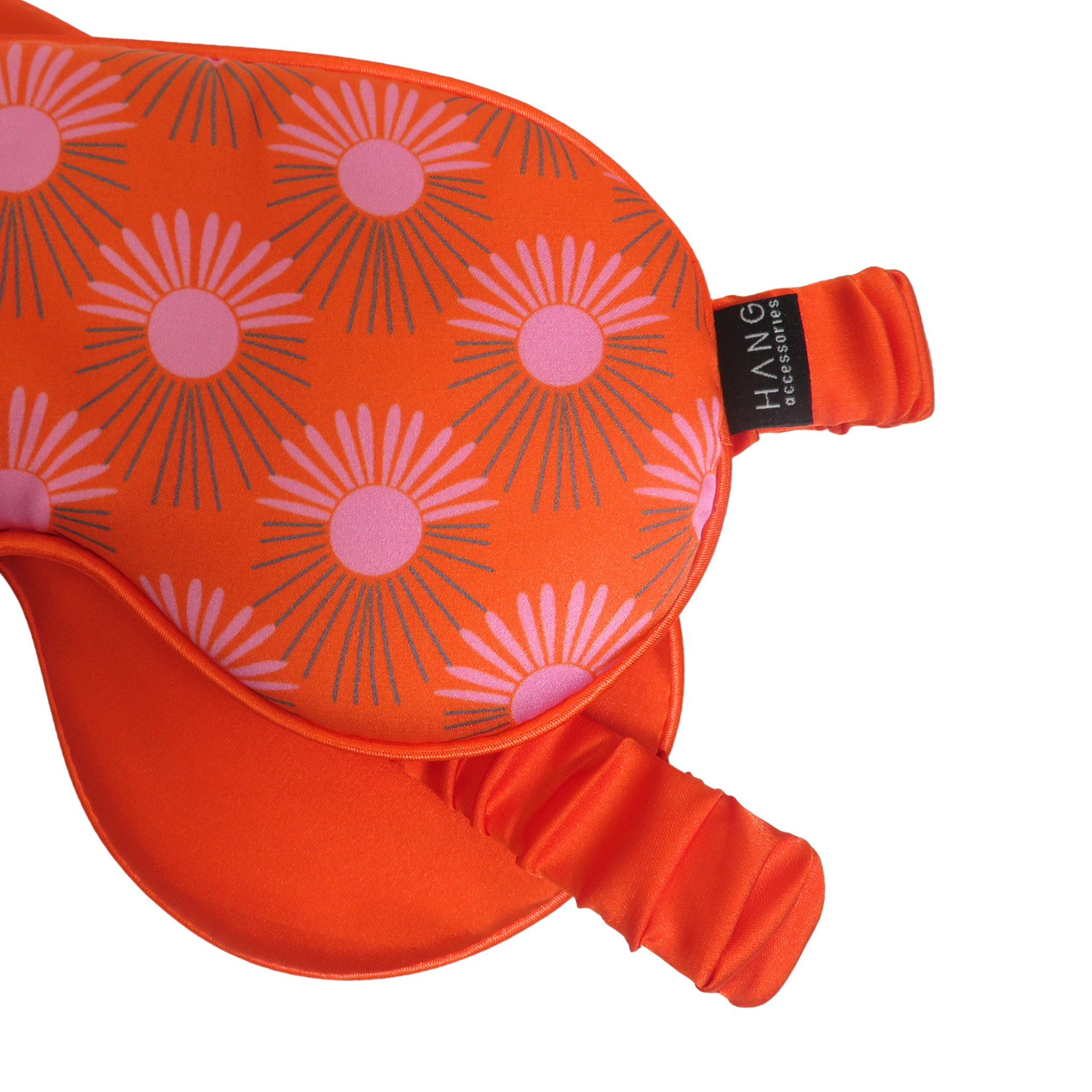 Close-up of an orange sleep mask with a pink and gray sunburst pattern.