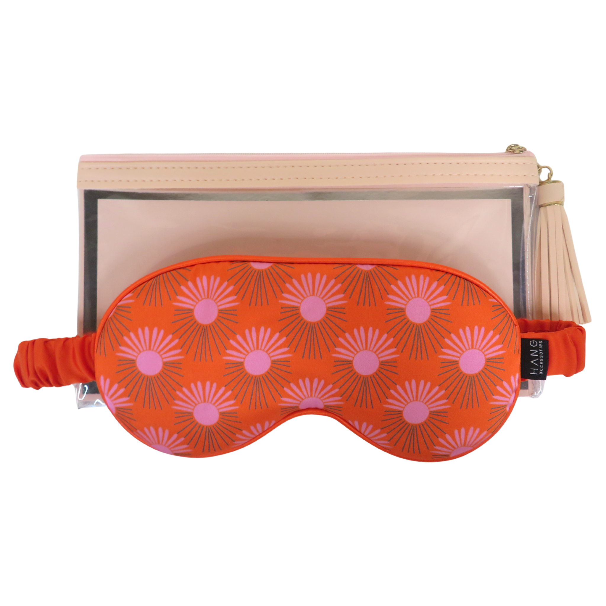 An red sleep mask with a pink sunburst pattern, displayed in front of a beige zippered pouch with a clear window and a tassel zipper pull on a white background.
