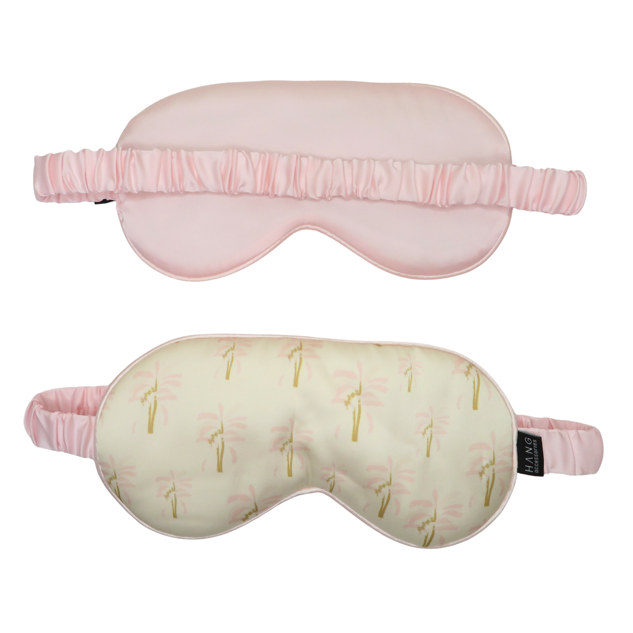 Two sleep masks shown on a plain white background: one solid pale pink mask above and one cream mask with a repeating pink and gold palm tree print below. Both have elastic straps.