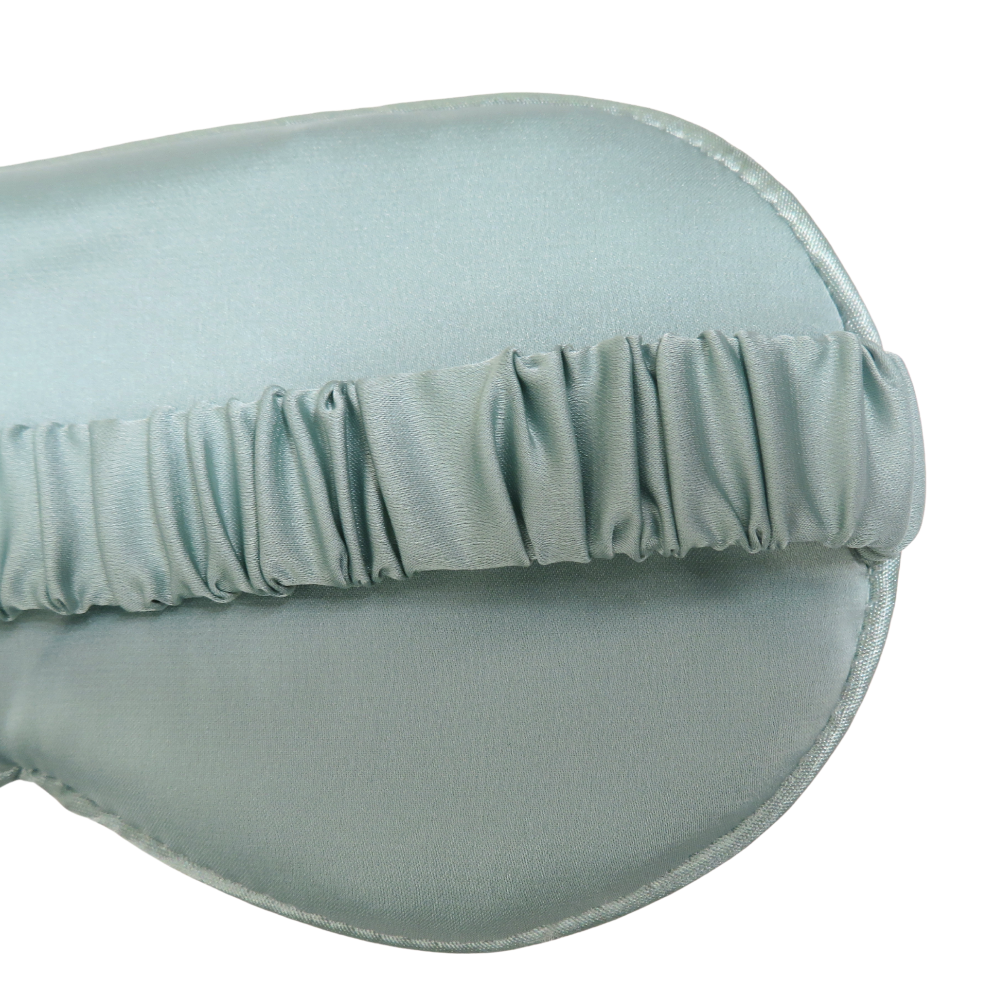A close-up of a light sage green satin sleep mask showing the gathered elastic strap against a plain white background.