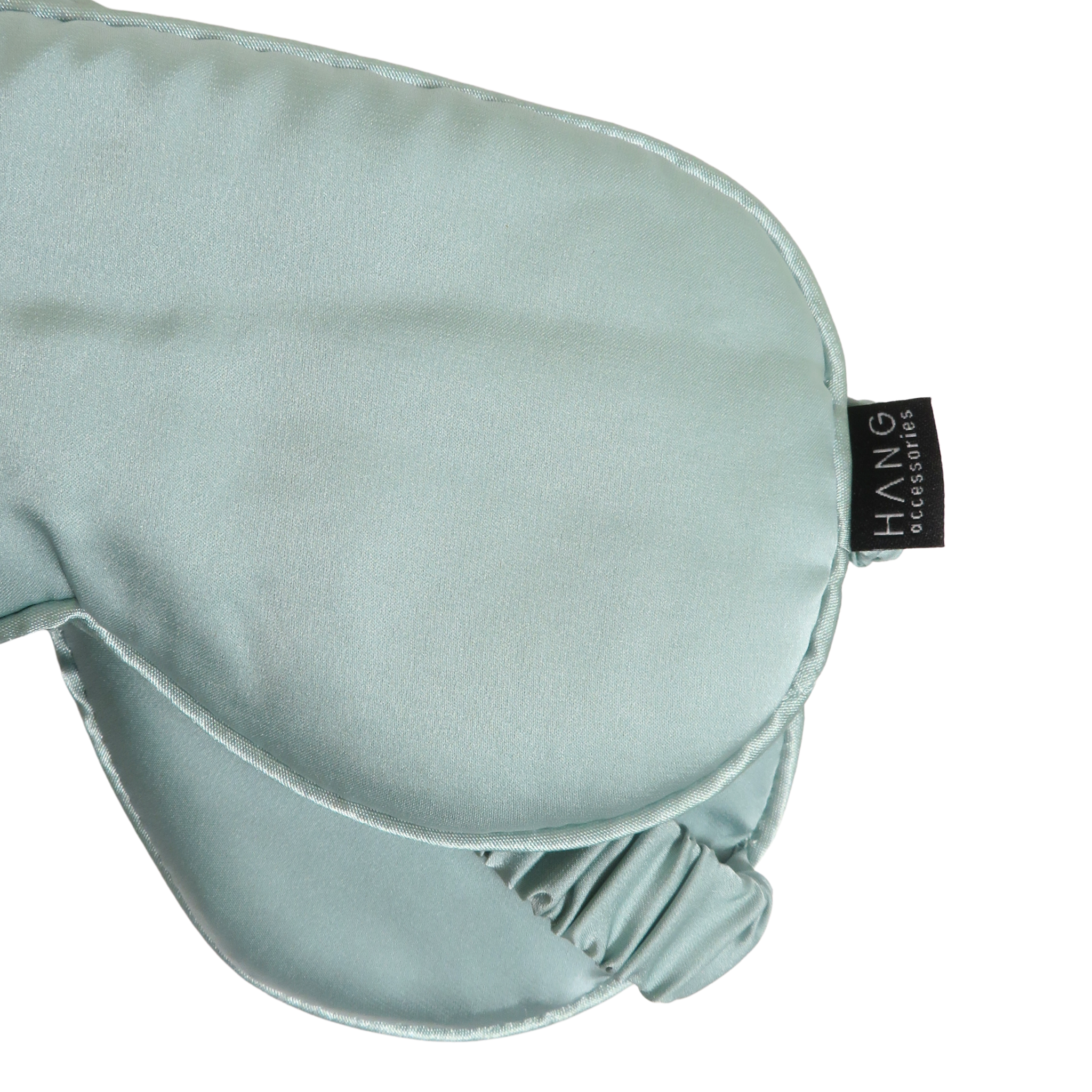 A close-up of a light sage green silk sleep mask with an elastic strap.